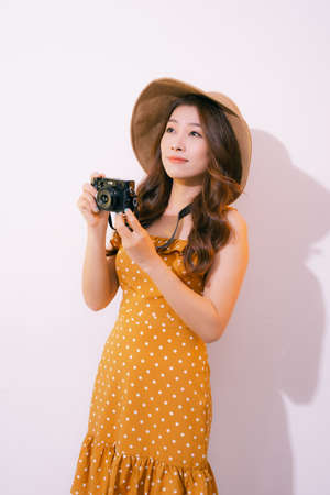 Pretty young tourist woman in summer white dress hat with photo camera isolated on pink background.の写真素材