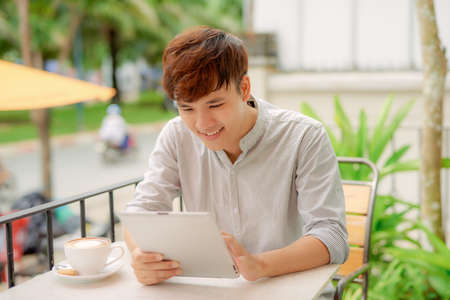 Front view portrait of a happy man holding tablet sitting in a coffee shopの写真素材