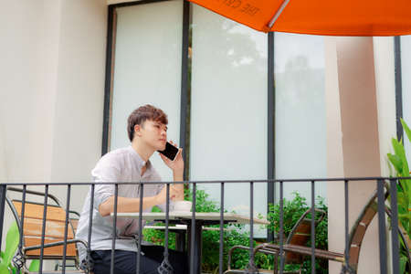 Young smiling man looking on the phone or reading message in cafe outdoorの写真素材