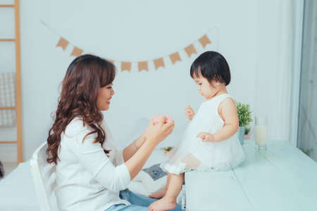 Beautiful young mother smiling while her baby daughter opening birthday gift box.の写真素材