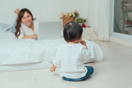 mother with laptop and her child on the bed in the morningの写真素材