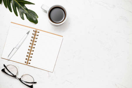 Top view of opened notebook for notes, pen, glasses and cup of coffee on white marble background.の写真素材