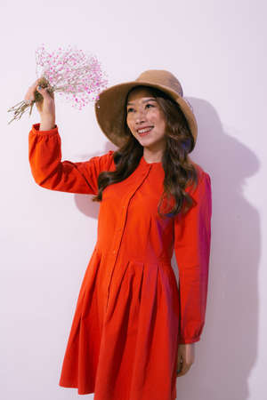 Young woman in straw hat and red dress holding pink flowers on pinkの写真素材