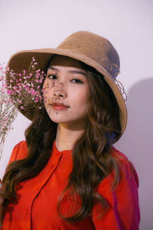 young asian woman in straw hat, smiling and holding flowers isolated on pinkの写真素材