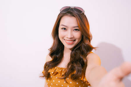 Young woman standing isolated on pastel background taking selfie photo on smartphone posing to camera smiling toothy close-upの写真素材