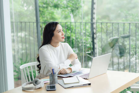 Young cheery happy positive cute beautiful business woman sit indoors in office using laptop computer.の写真素材