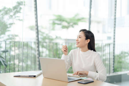 smiling happy beautiful asian woman relaxing using technology of laptop computer while sitting on tableの写真素材