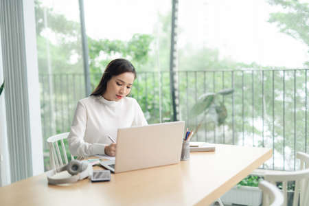 smiling happy beautiful asian woman relaxing using technology of laptop computer while sitting on tableの写真素材