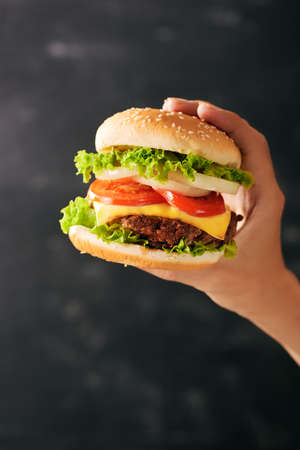 Tasty burger sandwich in hand isolated on black backgroundの写真素材