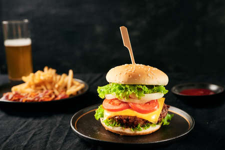 Fast food. A big burger with beef and a glass of beer. On a black backgroundの写真素材