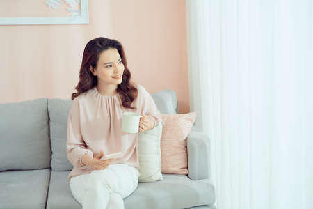 Cheerful young brunette holding a mug in bright living roomの写真素材