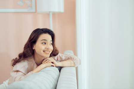Smiling relaxed attractive woman wearing glasses sitting on a sofa looking back over her shoulderの写真素材
