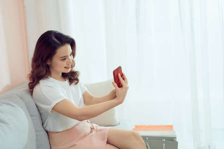 Smiling business woman taking photo using cell phone in home officeの写真素材