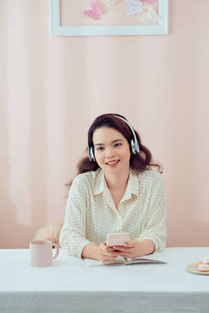 Image of serious beautiful woman using wireless headphones and cellphone while sitting at tableの写真素材
