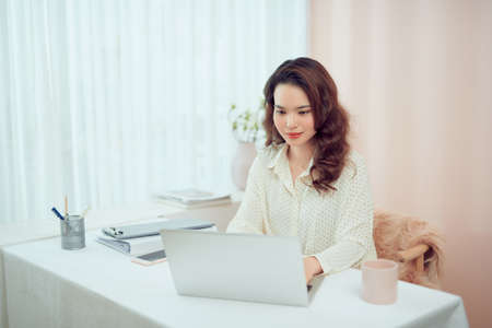 Beautiful young woman in casual clothing using laptop and smiling while working indoorsの写真素材