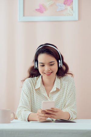 Happy woman at home wearing headphones watching videos on smart phoneの写真素材