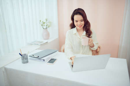 Asian female freelancer relaxing sitting with cup of coffee in front of laptopの写真素材