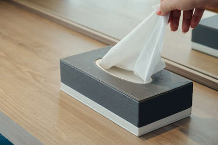 Closeup woman hand picking white tissue paper from tissue box on wooden tableの写真素材