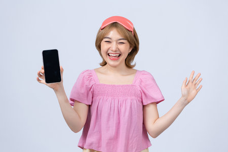 Young woman in pajamas jam sleep eye mask rest relaxing at home hold mobile phone blank screen workspace areaの写真素材