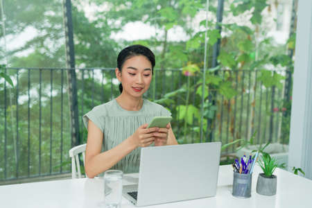 Happy young elegant businesswoman scrolling in smartphone while enjoying break by workplaceの写真素材