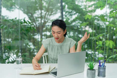 Unhappy young woman looking at laptop screen, irritated by bad gadget work, low internet connection, working remotely at home.の写真素材
