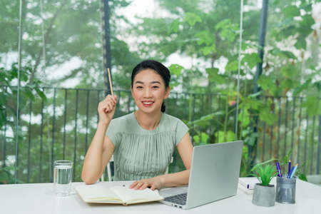 Business Asian young woman working with computer laptop holding pen and thinking to get ideas and requirementの写真素材
