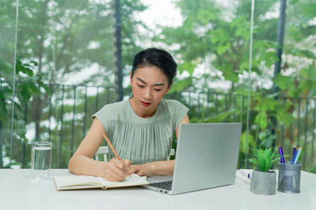 Busy businesswoman writing in an agenda on a desktop at officeの写真素材