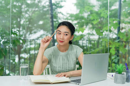 Business Asian young woman working with computer laptop holding pen and thinking to get ideas and requirementの写真素材