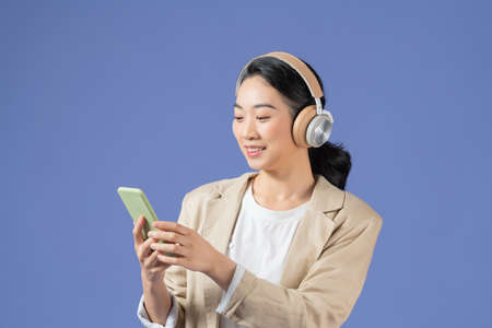 Half length of smiling young lady with headphones looking away while holding mobile phone in armの写真素材