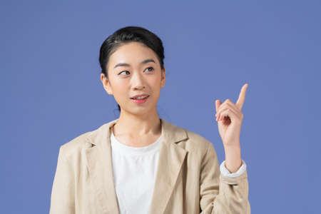 Portrait of happy young lady standing isolated over purple background and pointingの写真素材