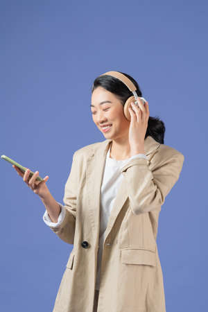Half length of smiling young lady with headphones looking away while holding mobile phone in armの写真素材