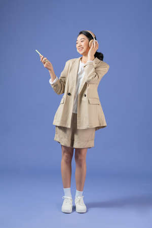 Image of young beautiful woman wearing headphones smiling and holding cellphone isolated over purple backgroundの写真素材
