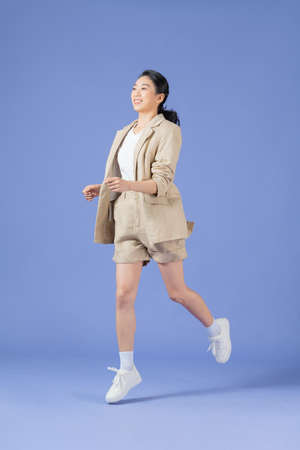 Full length body size photo of girlish cheerful woman jumping stepping smiling isolated purple backgroundの写真素材