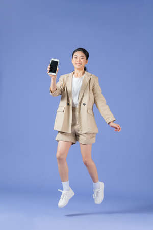Cheerful girl jumping up and newest smartphone showing empty screen, enjoying new application for mobile phoneの写真素材