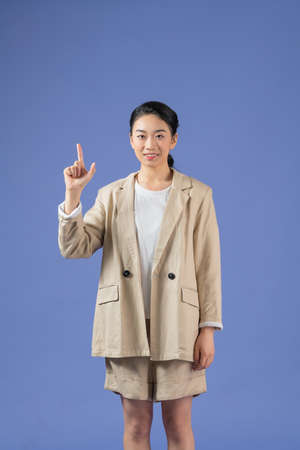 Smiling excited woman showing advertisement, pointing finger up, standing against purple background.の写真素材