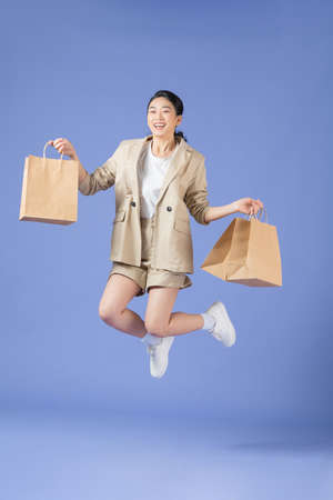 a smiling young girl holding shopping bags while jumping isolated over purple backgroundの写真素材