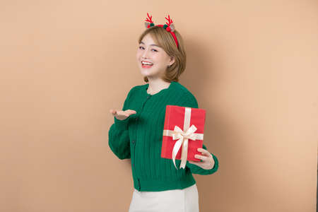 delighted funny young woman in a Christmas reindeer costume laughing with gift on beige backgroundの写真素材