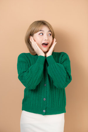 Happy Asian portrait beautiful cute young woman standing surprised excited screaming open mouth show hands isolated on beige background,の写真素材