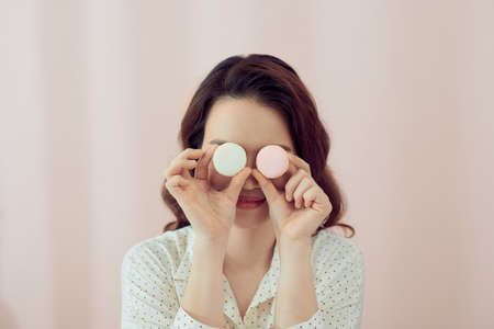 Young asian woman over isolated pastel pink background wearing colorful French macarons as glassesの写真素材