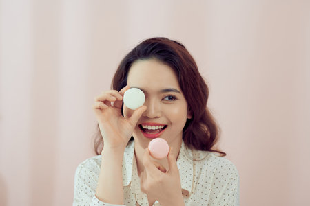 Young woman over isolated pink background holding colorful French macarons with funny faceの写真素材