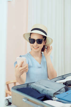 young woman preparing and packing clothes into suitcase on a bed at home, holiday travel conceptの写真素材