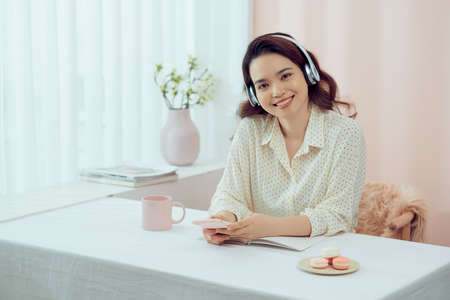 Woman with headphones and a diary eating macarons in living roomの写真素材