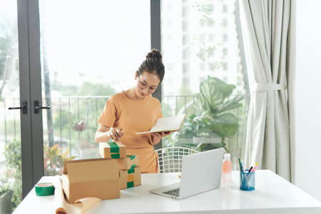 woman checking purchase order in laptop and write in the delivery on package box sell onlineの写真素材