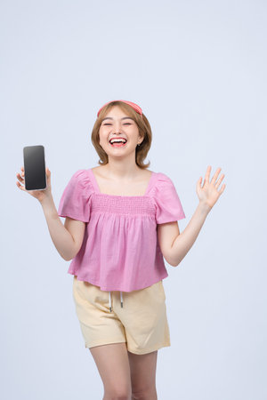 Happy smiling asian girl in pajamas and sleeping mask tracking her sleep with mobile app, showing smartphone screen and look pleased, white backgroundの写真素材