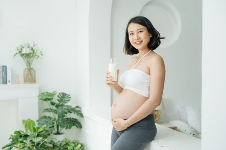 Beautiful pregnant woman drinking milk at homeの写真素材