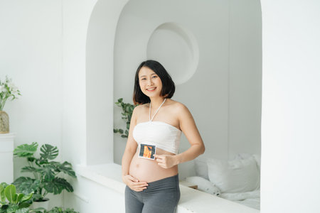 Cheerful pregnant woman holds ultrasound photo at her bellyの写真素材