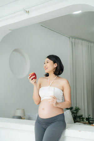 Pregnant Woman holding her pregnant belly and get a glass of milk and apple.の写真素材
