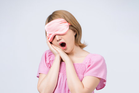 Tired bored girl with eye mask on head yawning cover wide open mouth with palm having close eyes going to sleep isolated on white backgroundの写真素材