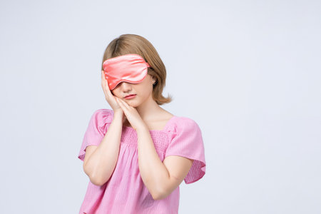 people and bedtime concept - happy young woman in pajama and eye sleeping mask over grey backgroundの写真素材