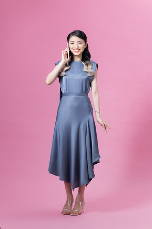 Beautiful young woman talking by mobile phone on pink backgroundの写真素材